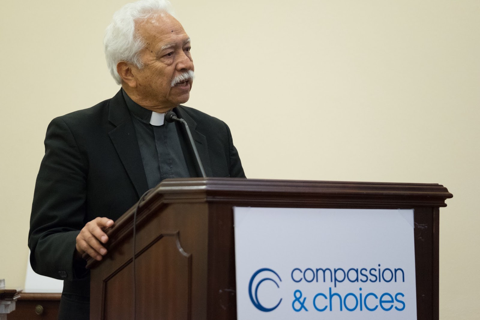 Reverend Castuera stands at a podium with a Compassion & Choices sign.