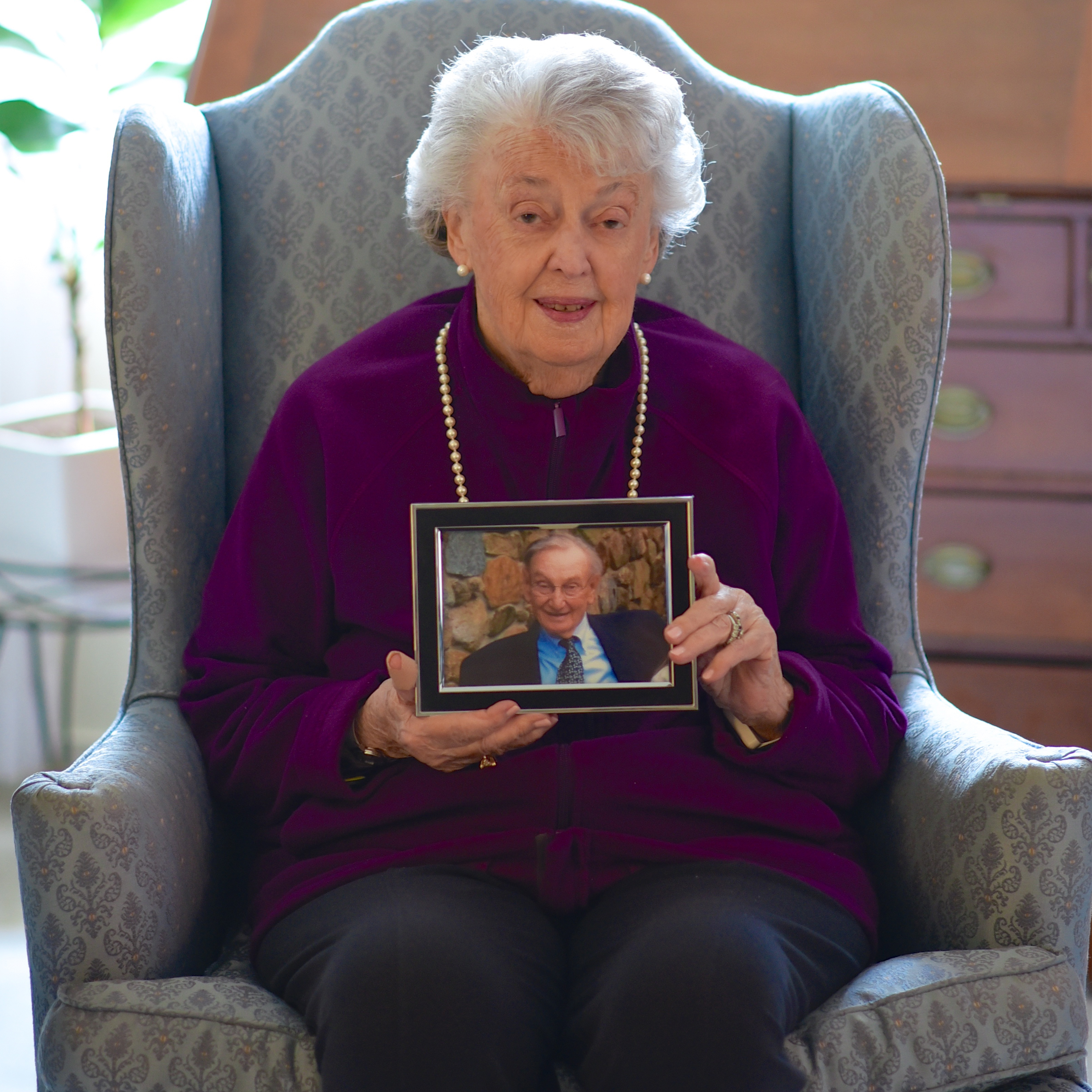Lauralyn Blanchard seated in a high back chair holding a picture of her late husband Bradford