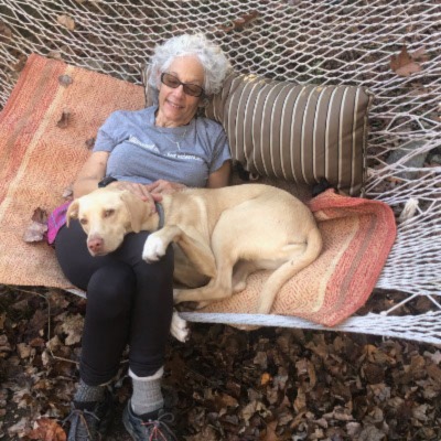Linda Rogen sits in a hammock with a yellow dog draped over her lap.